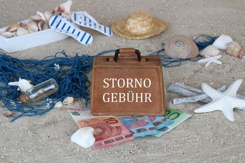 © Racamani - stock.adobe.com Foto: Sand, Muscheln, Geldscheine und Koffer mit Aufschrift Stornogebühr