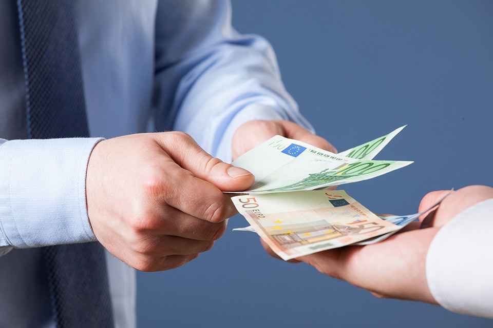 Foto: zwei Hände übergeben Geldscheine in eine dritte Hand